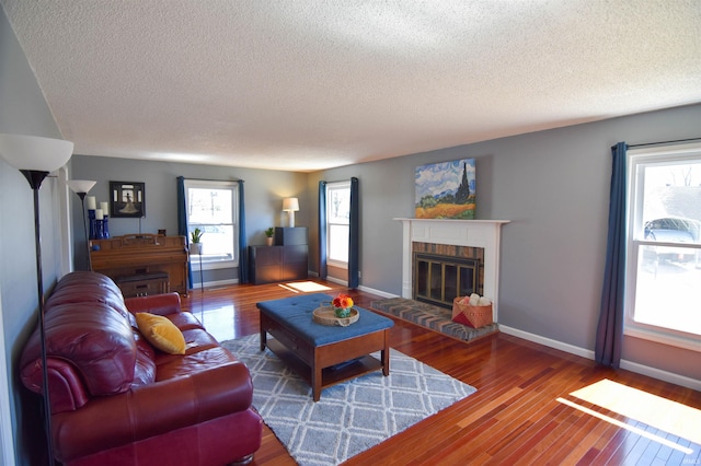 living room with baseboards, a textured ceiling, wood finished floors, and a fireplace