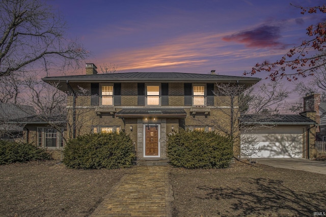 view of front of home with brick siding, concrete driveway, a chimney, metal roof, and a standing seam roof