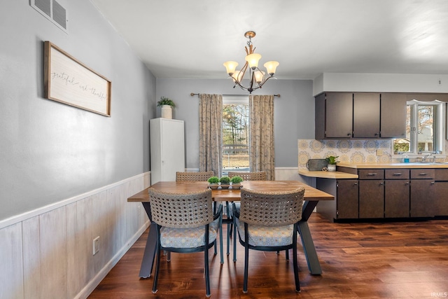 dining area with a wainscoted wall, a notable chandelier, visible vents, and dark wood-style floors