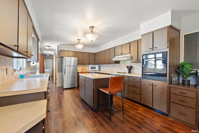 kitchen with white microwave, freestanding refrigerator, a sink, under cabinet range hood, and black oven