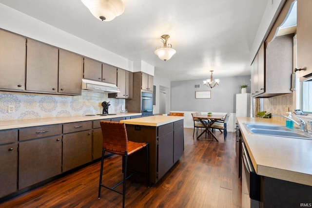 kitchen with a sink, under cabinet range hood, tasteful backsplash, dark wood finished floors, and light countertops