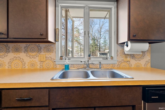 kitchen featuring dark brown cabinetry, dishwashing machine, light countertops, and a sink