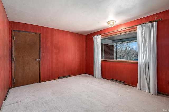 empty room featuring light carpet, visible vents, and wood walls