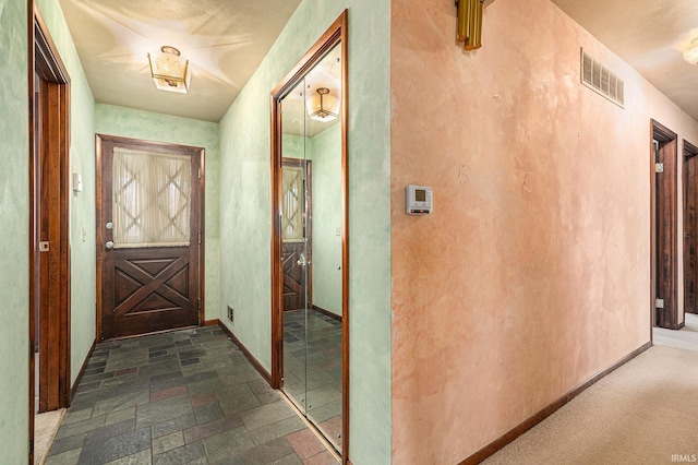 corridor with stone tile floors, visible vents, and baseboards