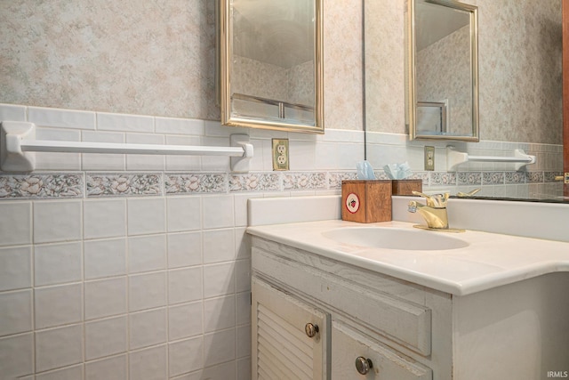 bathroom featuring wallpapered walls, tile walls, vanity, and wainscoting