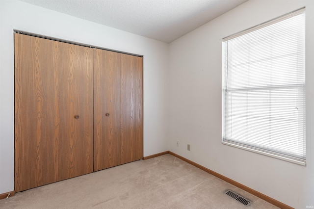 unfurnished bedroom with light carpet, visible vents, multiple windows, and a closet