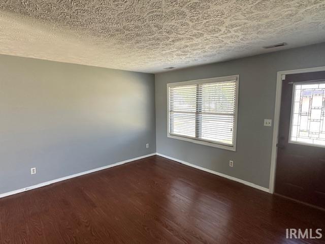 interior space with visible vents, a textured ceiling, baseboards, and wood finished floors