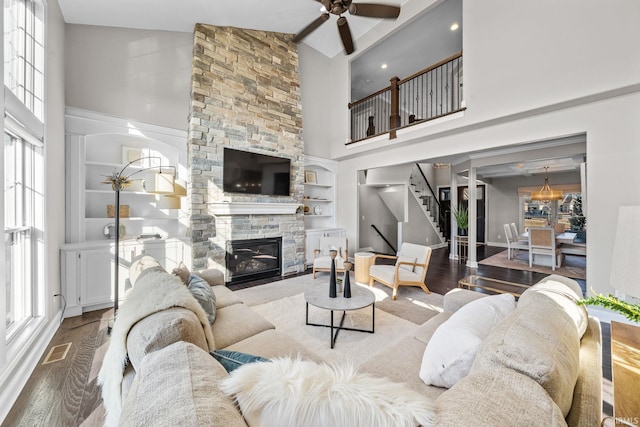 living area with visible vents, a stone fireplace, wood finished floors, and stairway