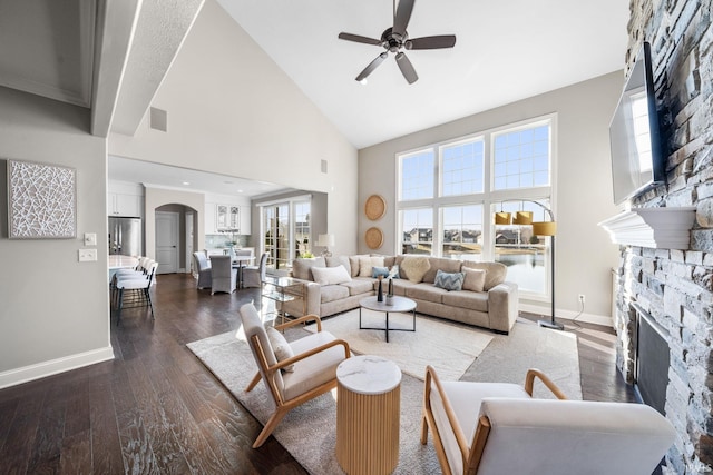 living area with visible vents, high vaulted ceiling, wood finished floors, a stone fireplace, and baseboards