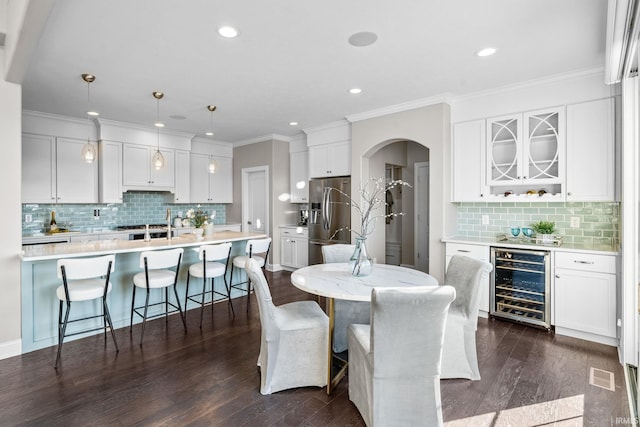 dining room featuring beverage cooler, visible vents, arched walkways, dark wood-style flooring, and ornamental molding