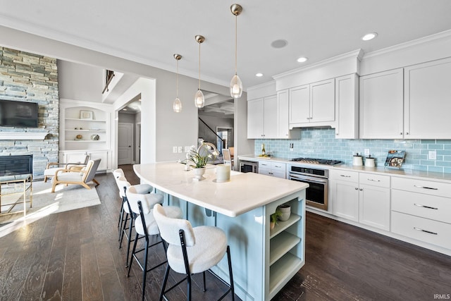 kitchen featuring a stone fireplace, appliances with stainless steel finishes, ornamental molding, and dark wood-style flooring