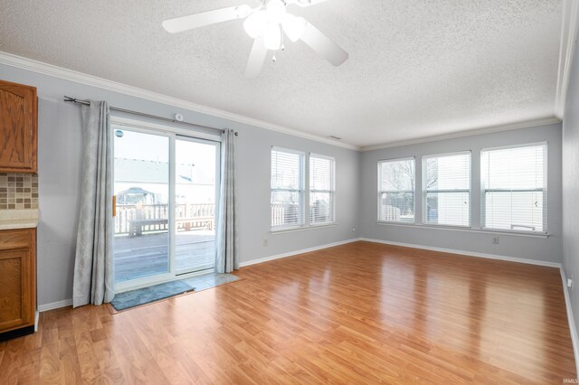 unfurnished living room with light wood-style flooring, a textured ceiling, baseboards, and ornamental molding