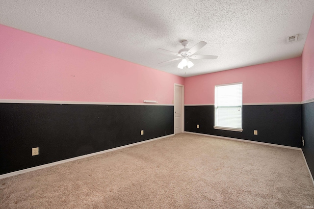 empty room featuring visible vents, ceiling fan, carpet, wainscoting, and a textured ceiling