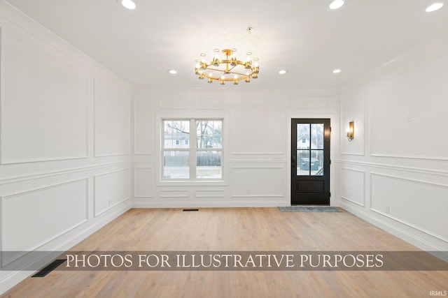 entrance foyer with visible vents, light wood finished floors, an inviting chandelier, ornamental molding, and a decorative wall