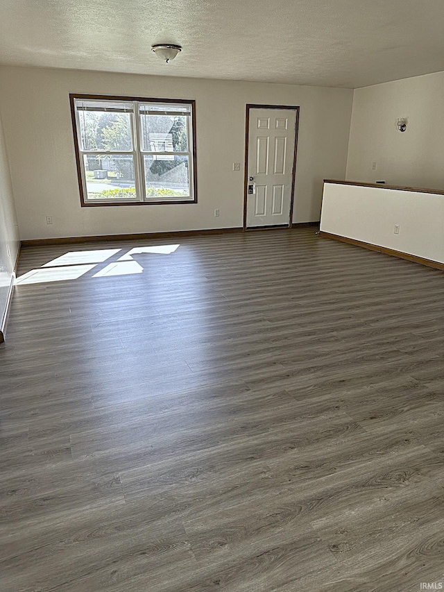 empty room with dark wood-style floors, a textured ceiling, and baseboards