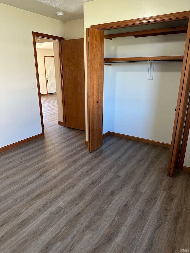 unfurnished bedroom with a closet, baseboards, and dark wood-style flooring