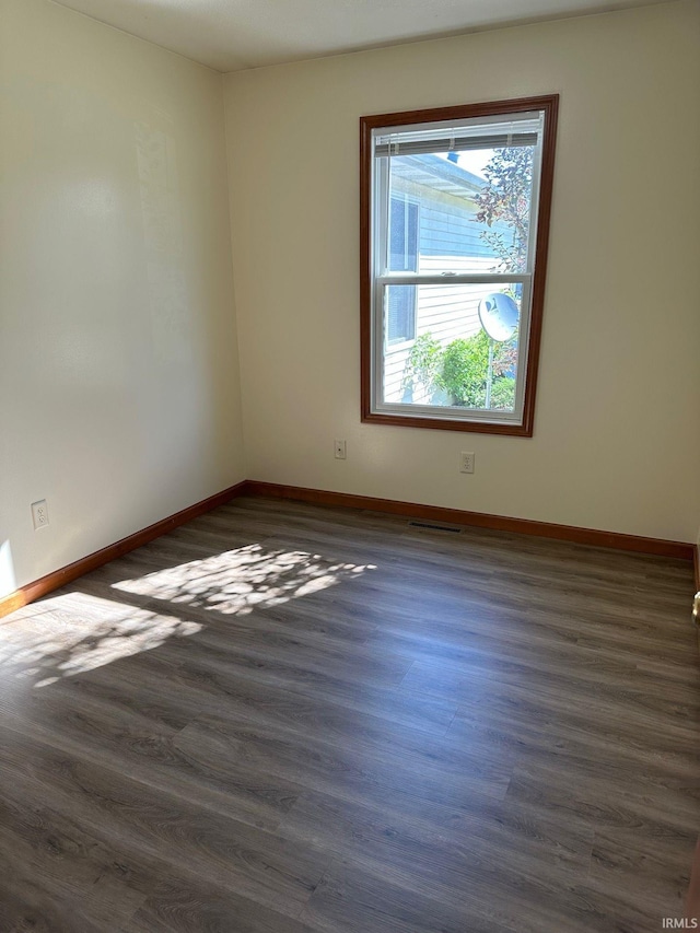 spare room with baseboards, visible vents, and dark wood-style flooring