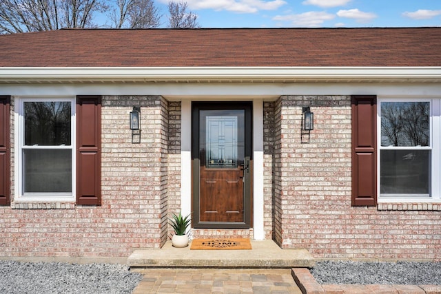 view of exterior entry with brick siding and a shingled roof