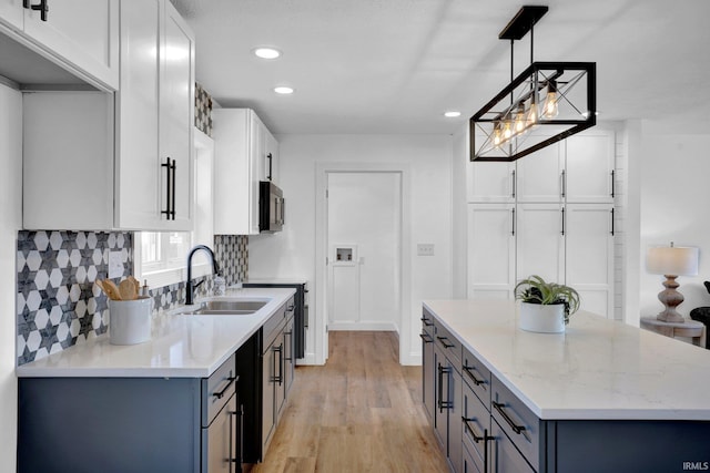 kitchen with a sink, stainless steel microwave, backsplash, light wood-style floors, and light stone countertops