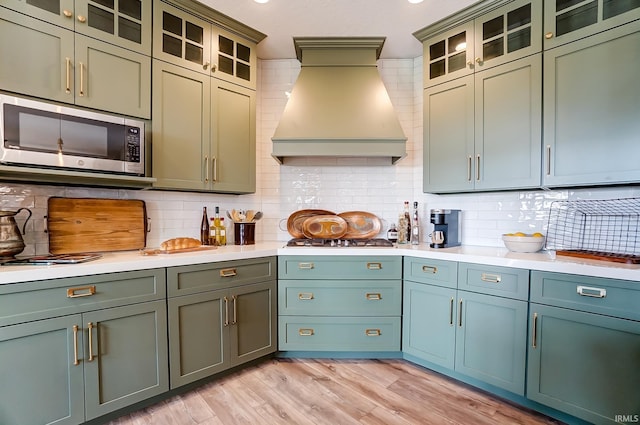 kitchen featuring tasteful backsplash, premium range hood, light countertops, light wood-style flooring, and appliances with stainless steel finishes