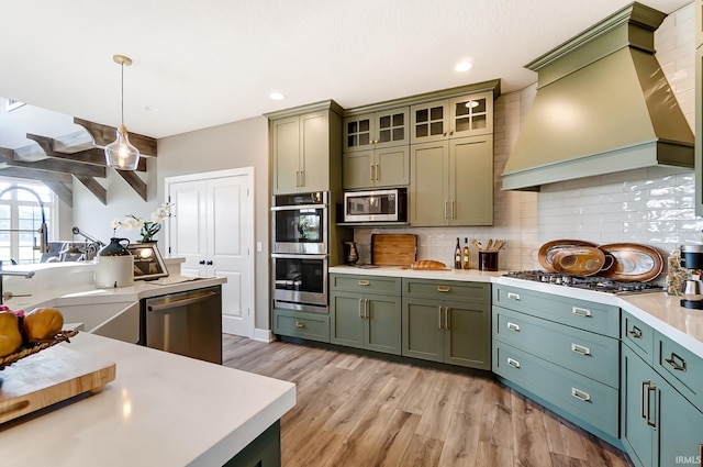 kitchen with green cabinetry, appliances with stainless steel finishes, light countertops, and premium range hood