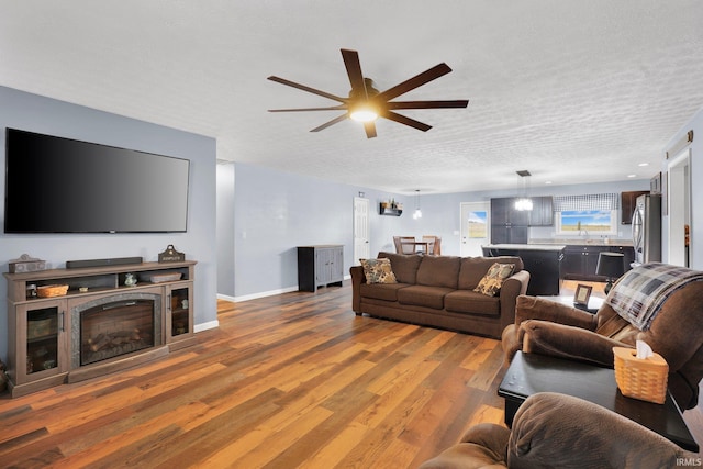 living room featuring a ceiling fan, wood finished floors, baseboards, a fireplace, and a textured ceiling