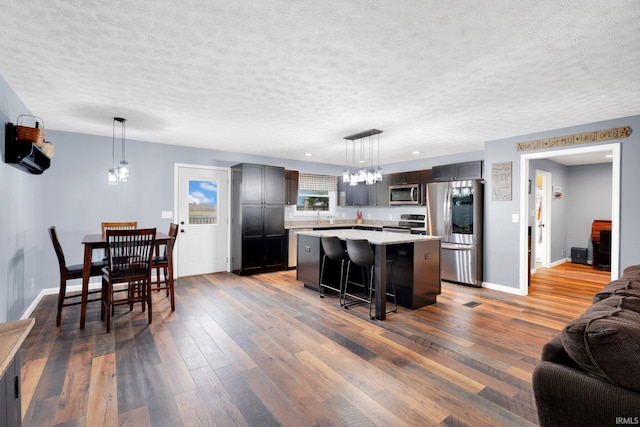 kitchen featuring wood finished floors, light countertops, appliances with stainless steel finishes, open floor plan, and a center island