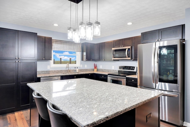 kitchen with a sink, light stone counters, a kitchen island, appliances with stainless steel finishes, and light wood finished floors