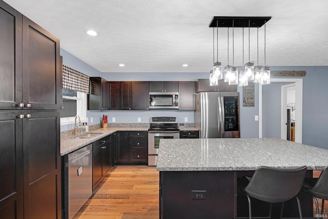 kitchen with a sink, a kitchen island, appliances with stainless steel finishes, light wood finished floors, and light stone countertops