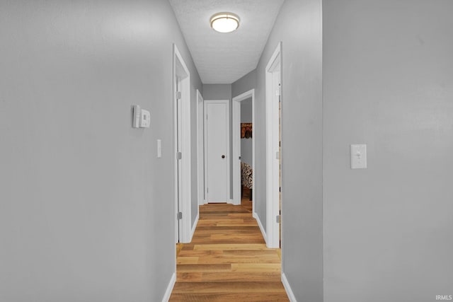 corridor with baseboards, a textured ceiling, and light wood finished floors