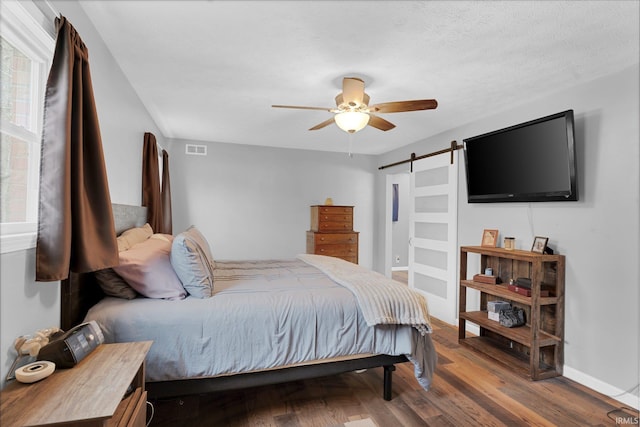 bedroom featuring a ceiling fan, wood finished floors, visible vents, baseboards, and a barn door