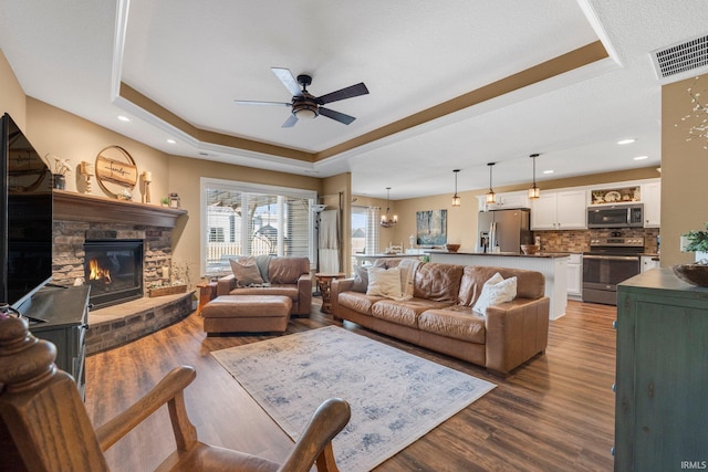 living area featuring visible vents, a fireplace, a raised ceiling, and wood finished floors