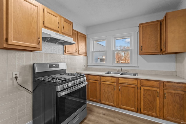 kitchen with under cabinet range hood, light countertops, light wood-style flooring, stainless steel gas range, and a sink