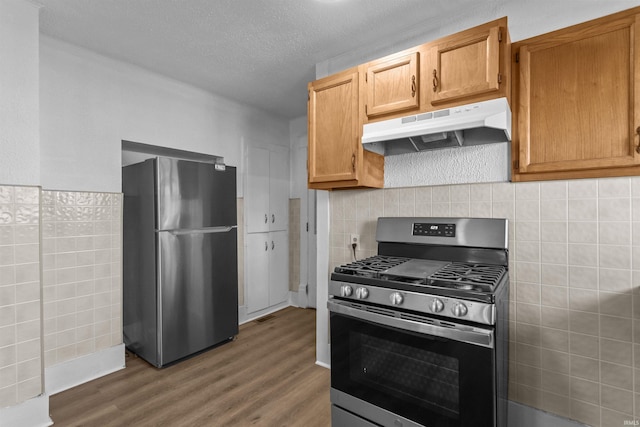 kitchen featuring tile walls, under cabinet range hood, stainless steel appliances, wood finished floors, and a textured ceiling