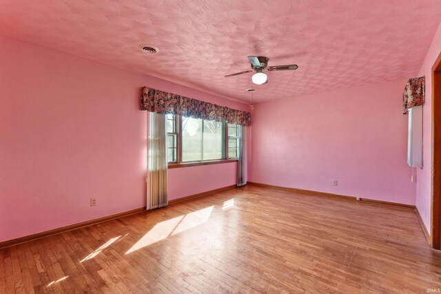 spare room with visible vents, a textured ceiling, light wood-style floors, baseboards, and ceiling fan