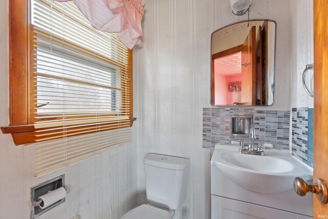 half bathroom with vanity, decorative backsplash, and toilet