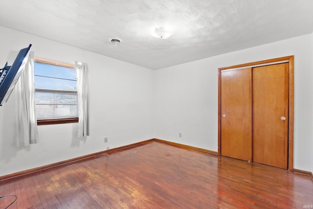 unfurnished bedroom with a closet, visible vents, baseboards, and hardwood / wood-style flooring