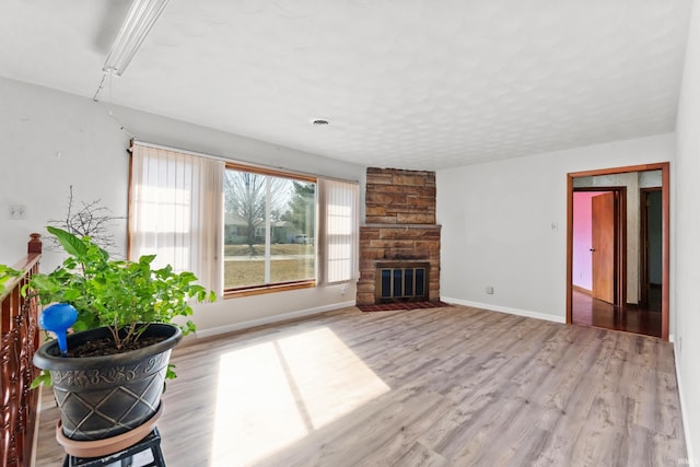 unfurnished living room featuring baseboards, a textured ceiling, a stone fireplace, and wood finished floors