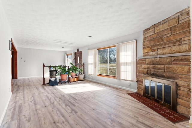 unfurnished living room featuring a stone fireplace, a textured ceiling, baseboards, and wood finished floors