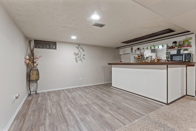 bar featuring wood finished floors, visible vents, black microwave, a textured ceiling, and a dry bar