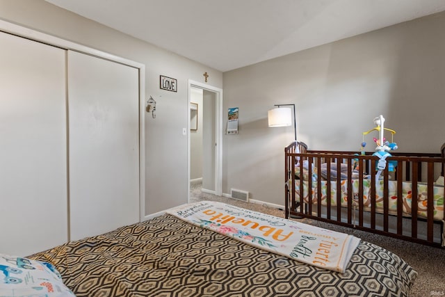 bedroom with a closet, visible vents, a crib, and baseboards