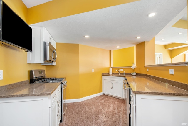 kitchen with a peninsula, a sink, white cabinets, appliances with stainless steel finishes, and light colored carpet