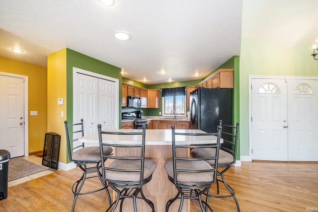 kitchen featuring baseboards, a breakfast bar, light wood-style flooring, a sink, and black appliances