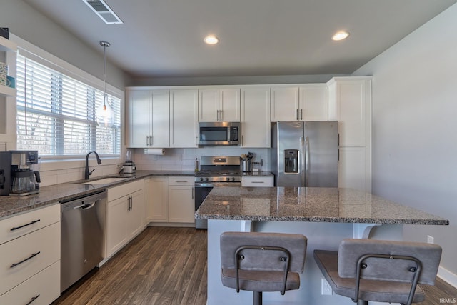 kitchen featuring a sink, a kitchen breakfast bar, tasteful backsplash, dark wood finished floors, and appliances with stainless steel finishes