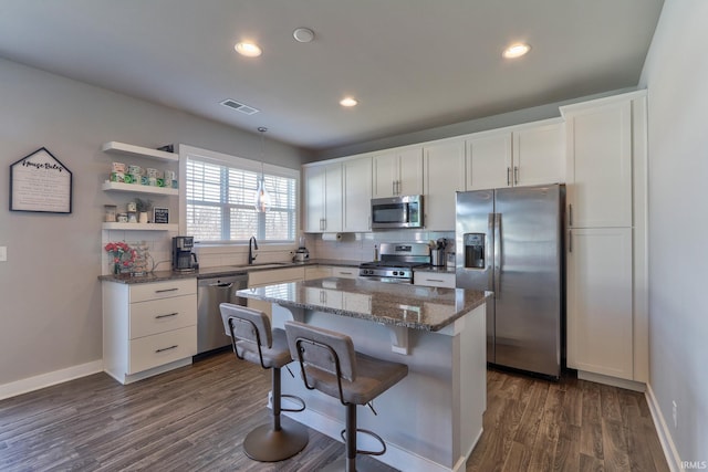 kitchen featuring dark wood-style floors, visible vents, stainless steel appliances, white cabinets, and a kitchen bar