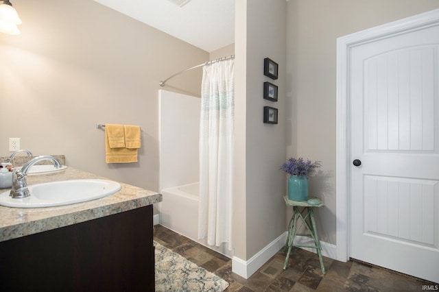 bathroom featuring baseboards, double vanity, a sink, shower / bath combination with curtain, and stone finish flooring