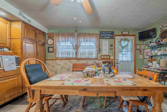 dining space with a textured ceiling, ceiling fan, and wallpapered walls