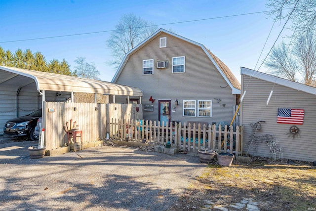 back of property with a gambrel roof, an AC wall unit, and fence