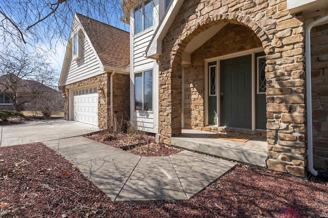 doorway to property featuring a garage, stone siding, roof with shingles, and concrete driveway