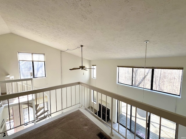 hallway with visible vents, lofted ceiling, a healthy amount of sunlight, and dark carpet